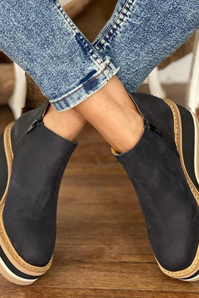 Front view of a woman standing in khaki Elara casual wedge ankle boots, paired with a casual skirt ensemble.
