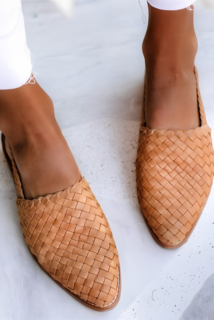 Woman wearing light brown Elara handcrafted moccasins, styled with casual trousers, walking outdoors on a sunny day, full body shot.