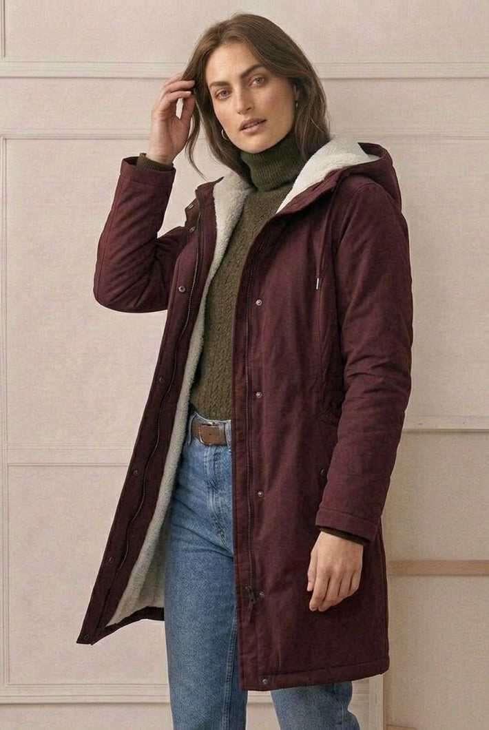 Model wearing the forest green Elara waterproof parka in an outdoor, rainy urban setting.