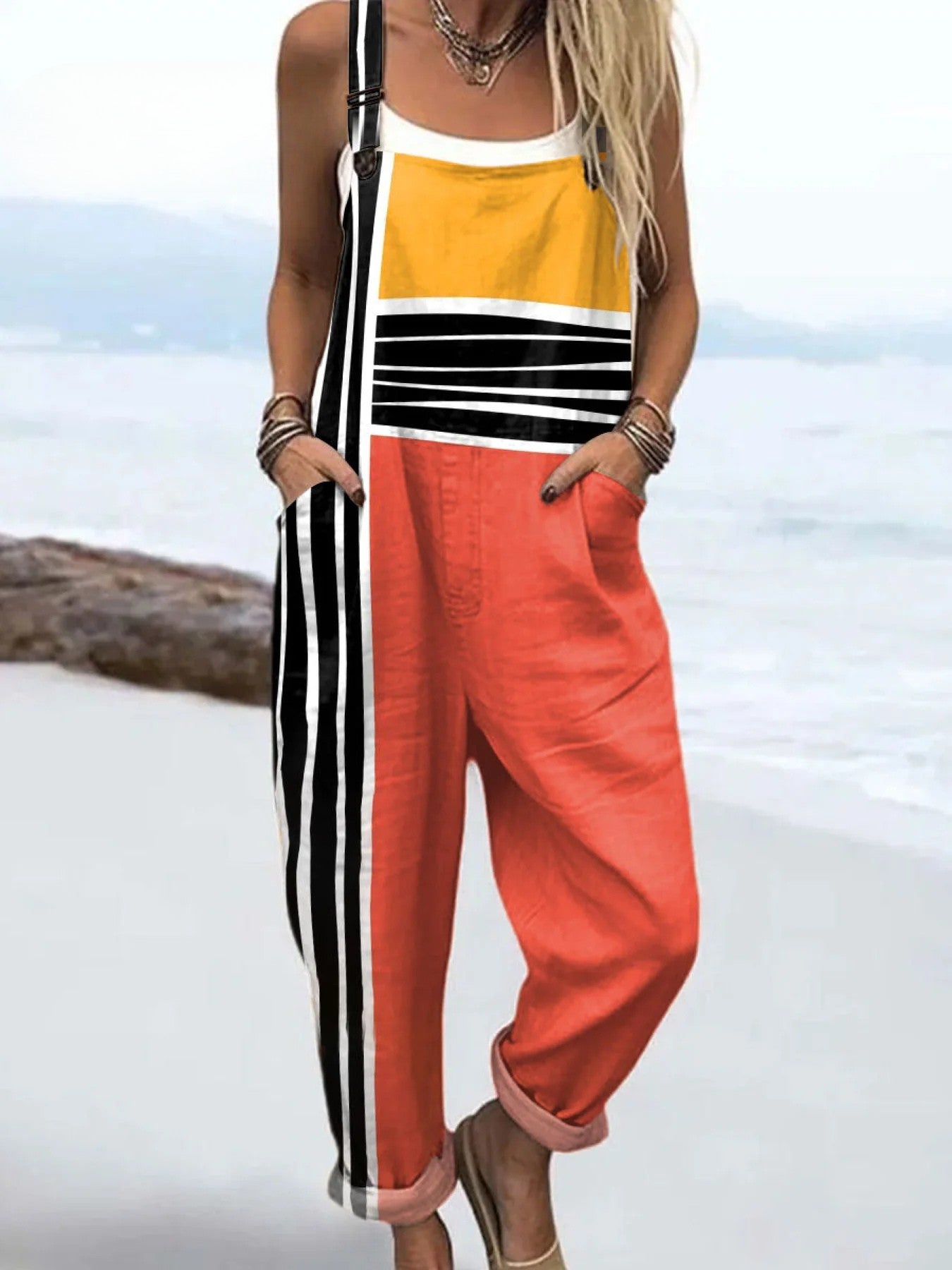 Front view of the Hadley color block jumpsuit featuring mustard yellow top, coral red mid-section, and black and white striped pants with deep pockets, worn by a model against a neutral background.