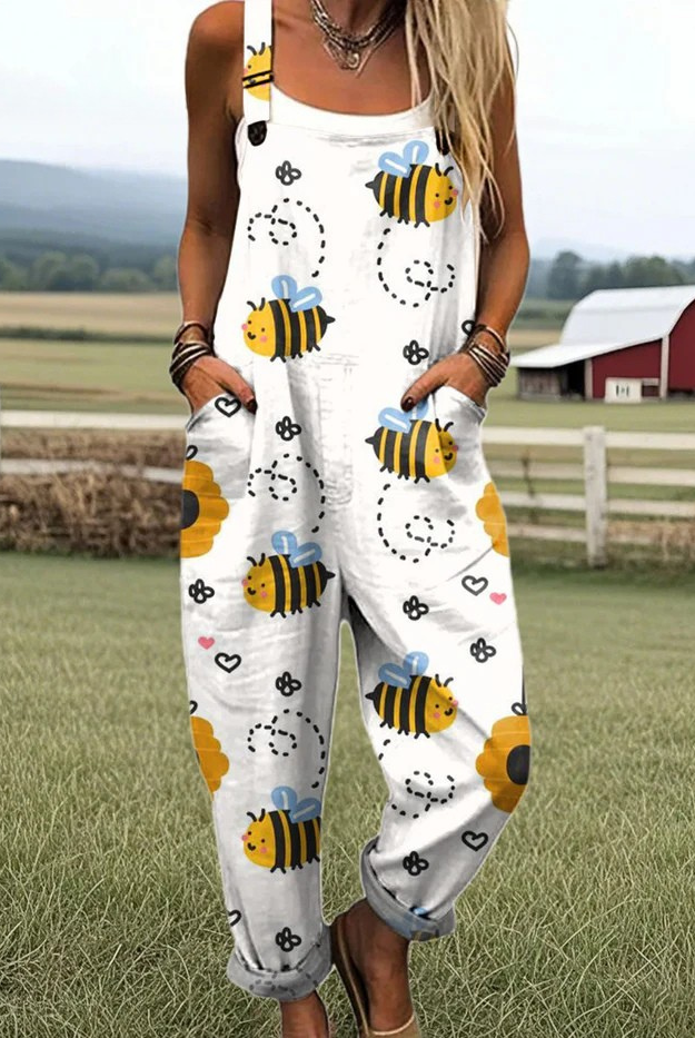 Front view of the Juniper Jumpsuit, a white overall adorned with a delightful pattern of yellow bees, red hearts, and vibrant sunflowers, showcasing its relaxed fit and rolled cuff hem.