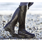 Model wearing green Calliope orthopedic leather boots while standing comfortably outdoors on a paved path.