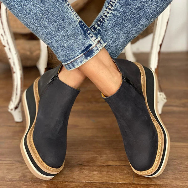 Front view of a woman standing in khaki Elara casual wedge ankle boots, paired with a casual skirt ensemble.