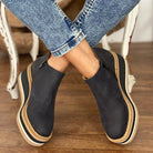 Front view of a woman standing in khaki Elara casual wedge ankle boots, paired with a casual skirt ensemble.