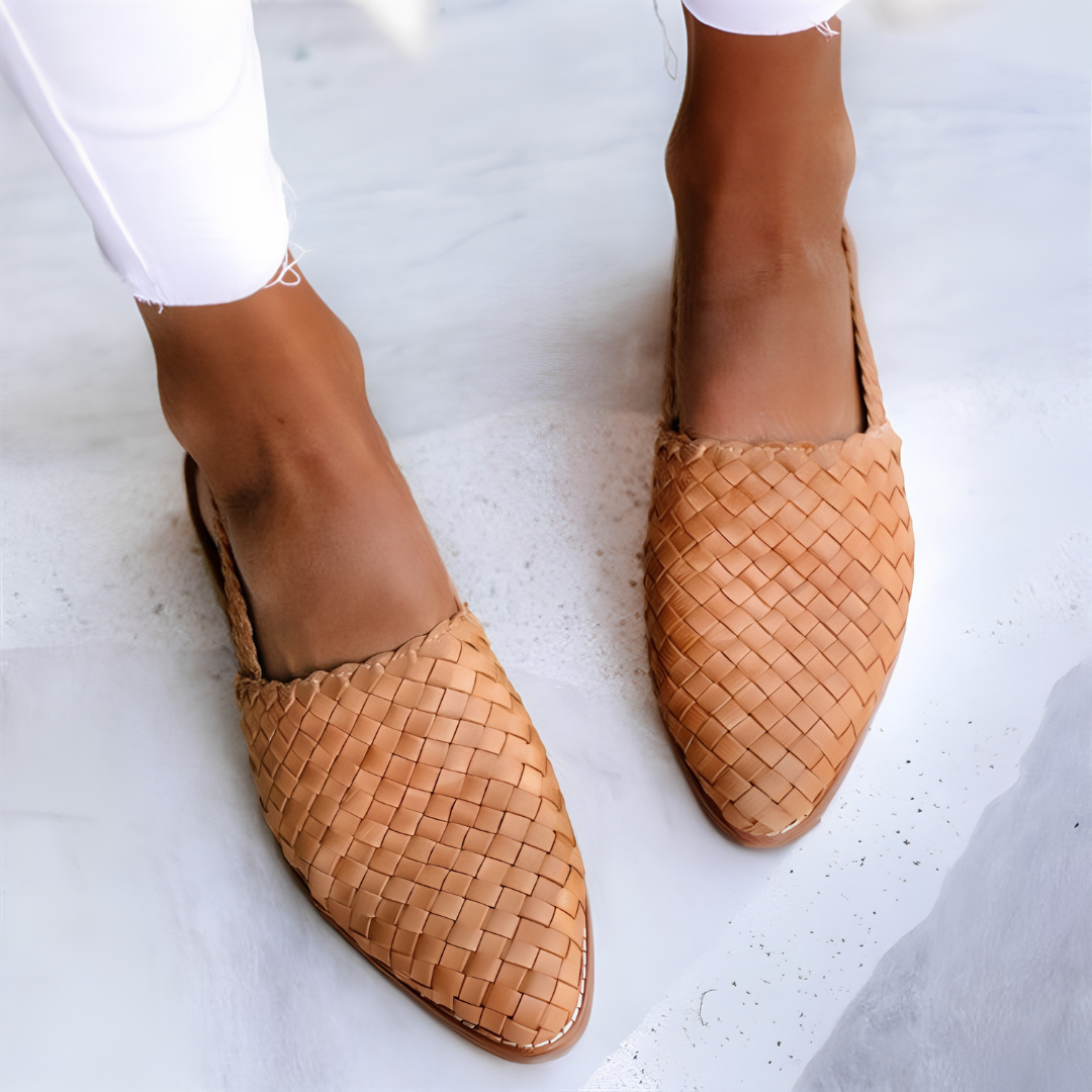 Woman wearing light brown Elara handcrafted moccasins, styled with casual trousers, walking outdoors on a sunny day, full body shot.