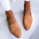 Woman wearing light brown Elara handcrafted moccasins, styled with casual trousers, walking outdoors on a sunny day, full body shot.