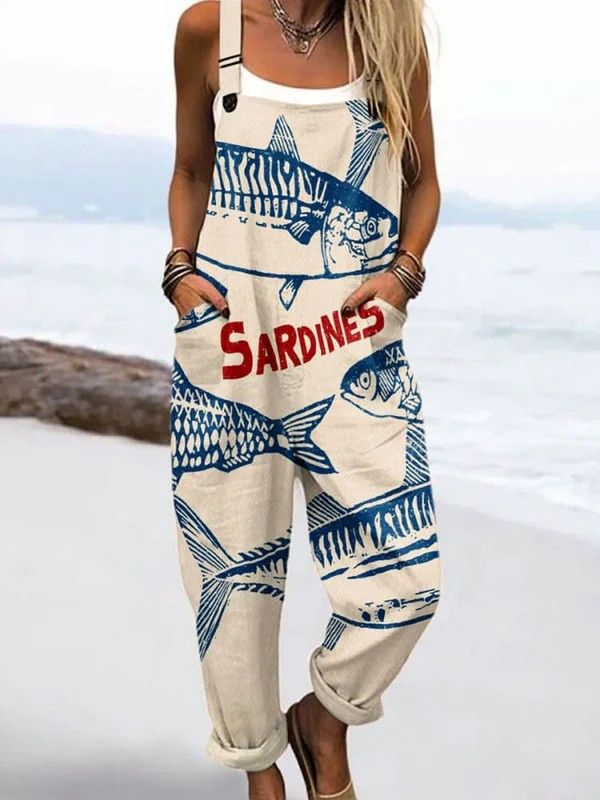 Front view of the Seraphina artistic graphic jumpsuit in cream with large blue sardine illustrations and red text, showcasing its relaxed fit and deep pockets.