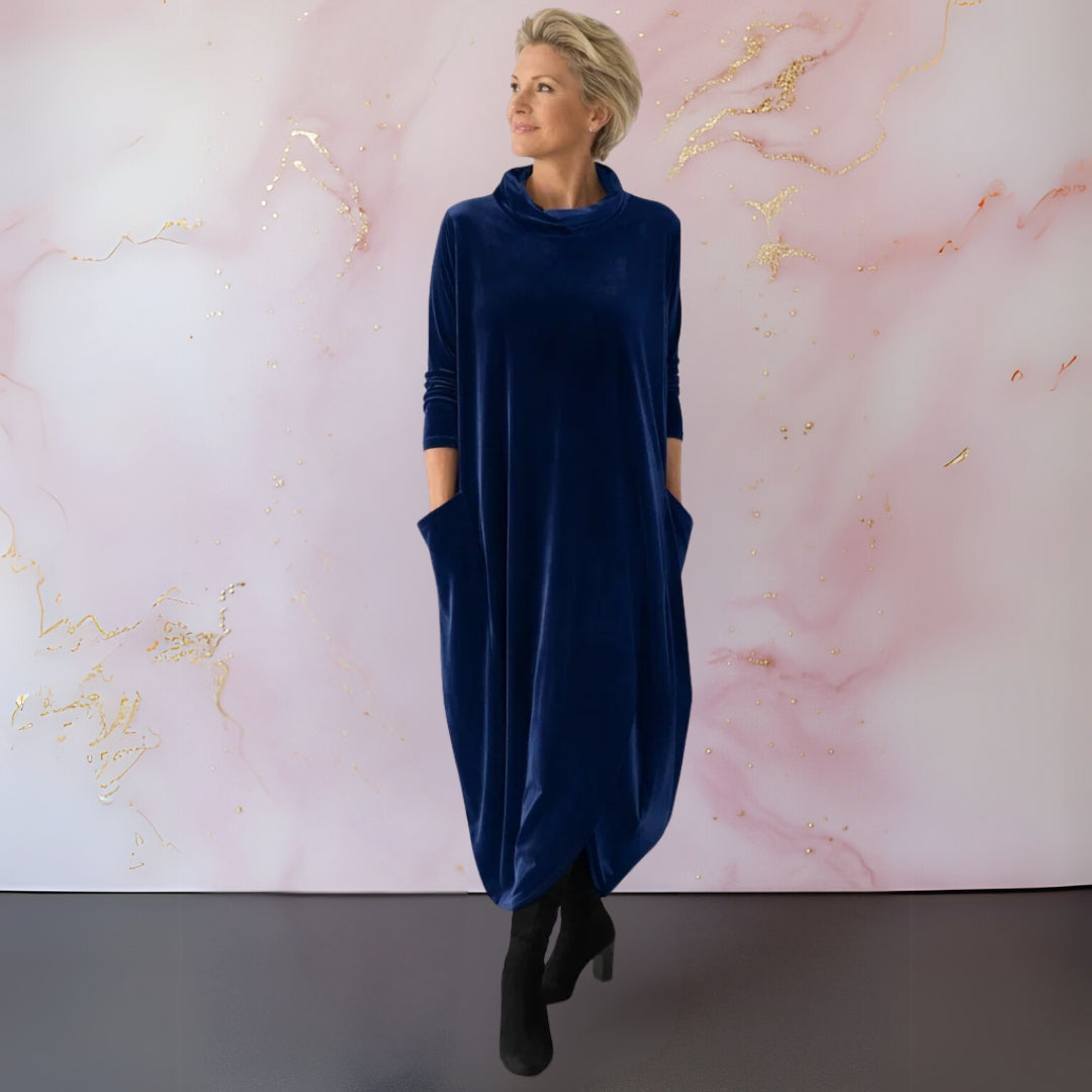 Side profile of a woman in a blue velvet maxi dress, highlighting the flowing design and practical side pockets.