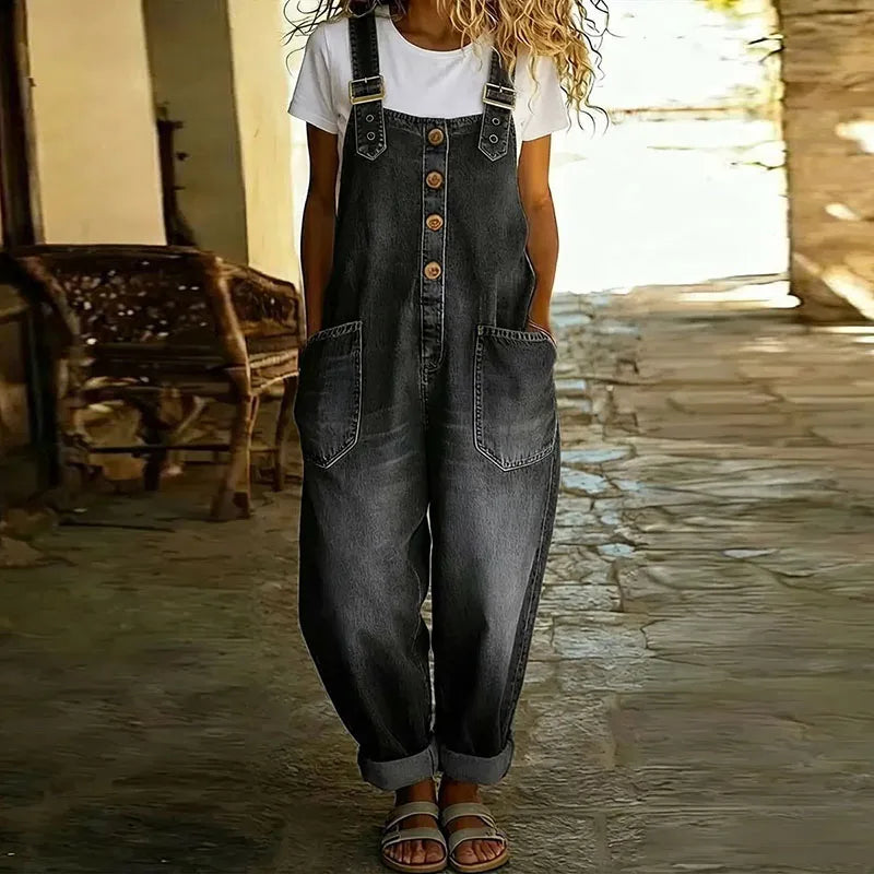 Lifestyle shot of a woman comfortably seated outdoors, wearing the Hadley soft denim overalls, illustrating ease of movement.