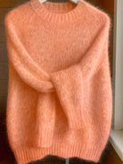 Lifestyle image of a woman enjoying a cup of coffee while wearing the orange Lila cashmere-blend sweater.